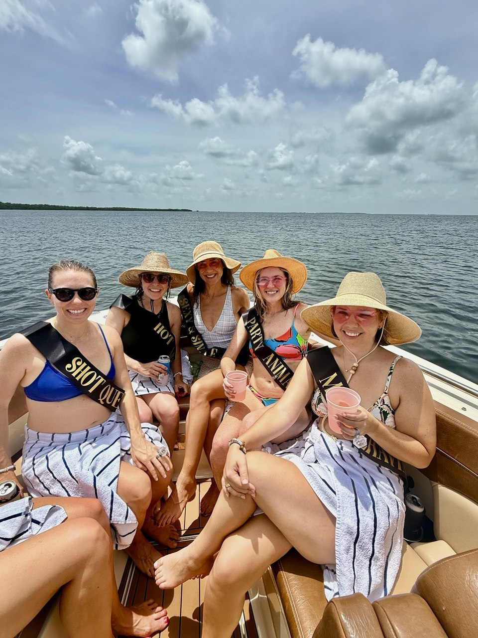 Friends celebrating aboard The Bougie Girl in sun hats and party sashes