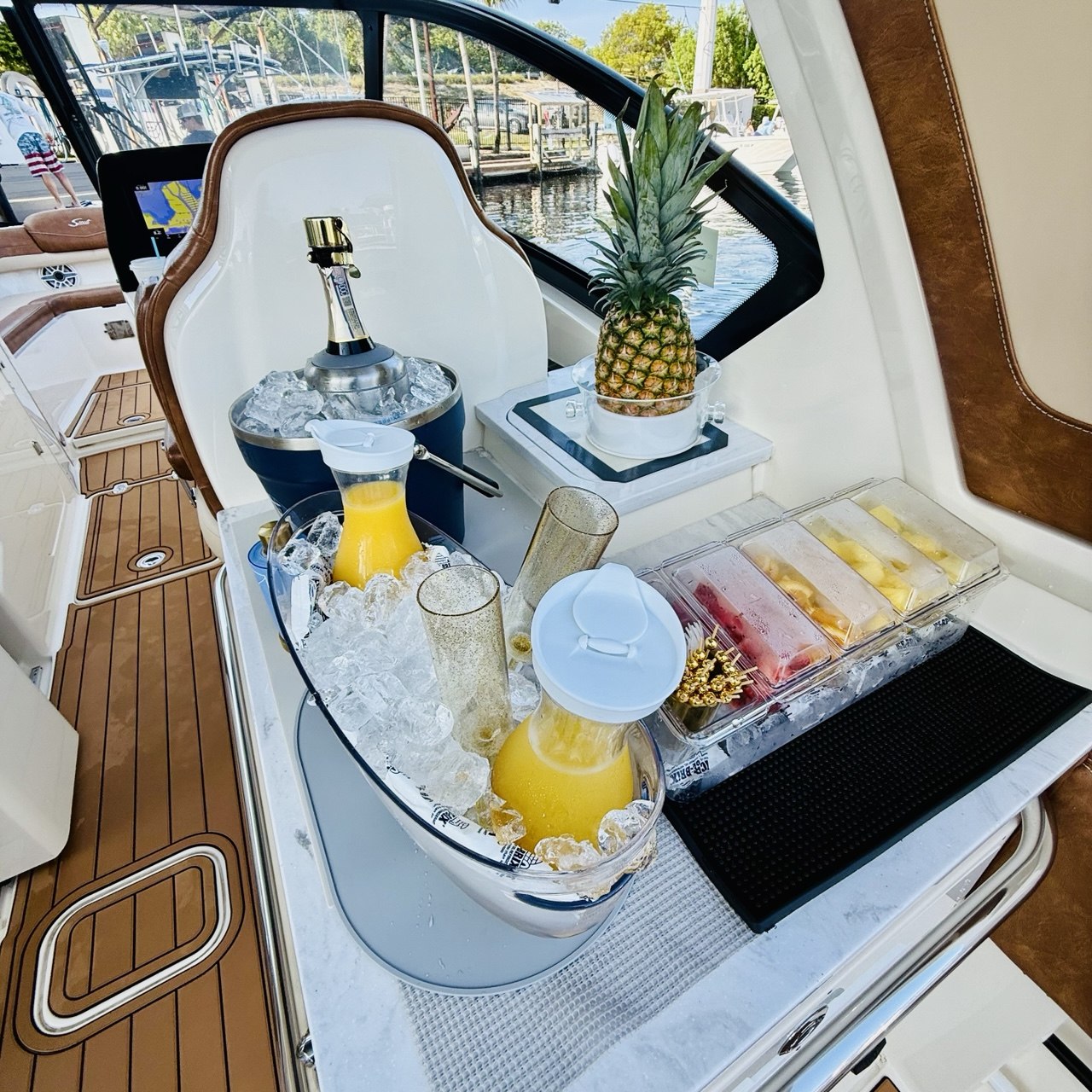 Onboard mimosa setup with chilled juices, champagne bucket, pineapple, and fruit garnishes aboard The Bougie Girl