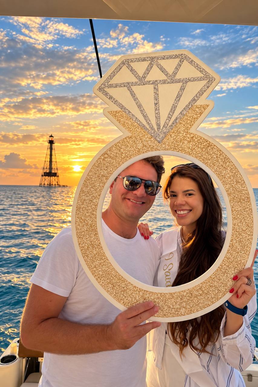 Couple celebrating their engagement at sunset with a ring photo prop by Alligator Reef Lighthouse