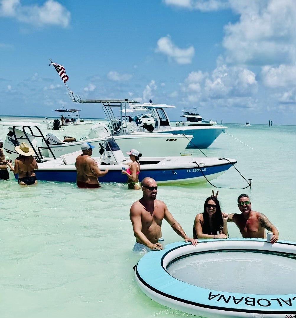 Guests enjoying turquoise sandbar water beside a floating lounge and anchored boats